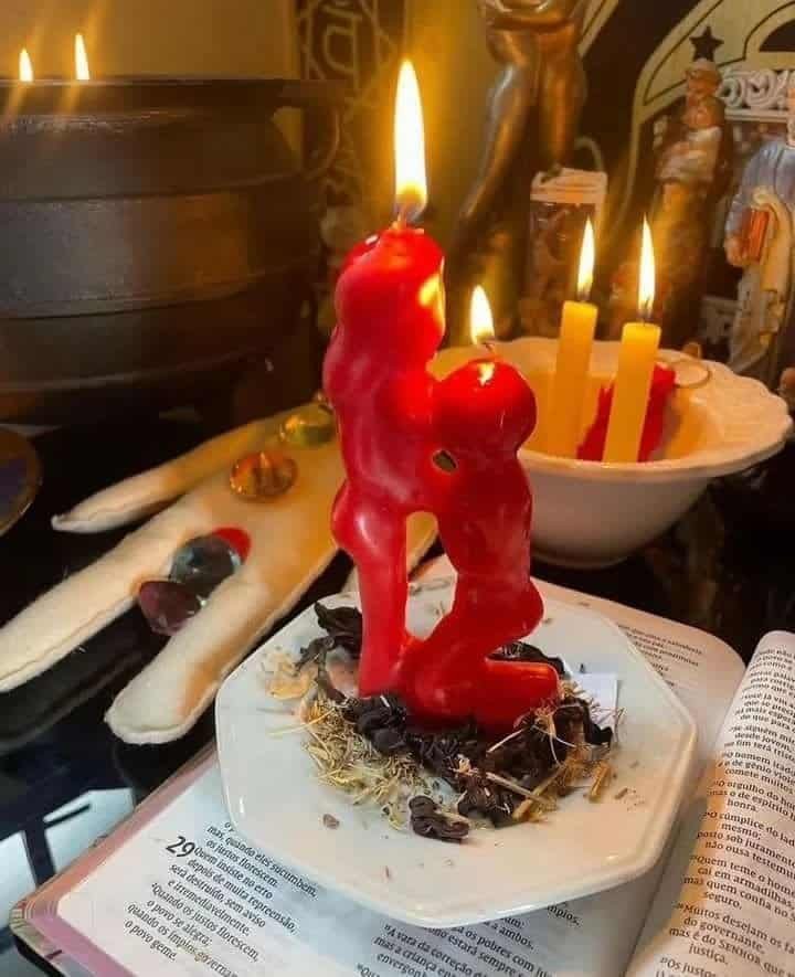 Ritual de amarre con vela roja en forma de pareja abrazada, acompañado de hierbas y elementos esotéricos
